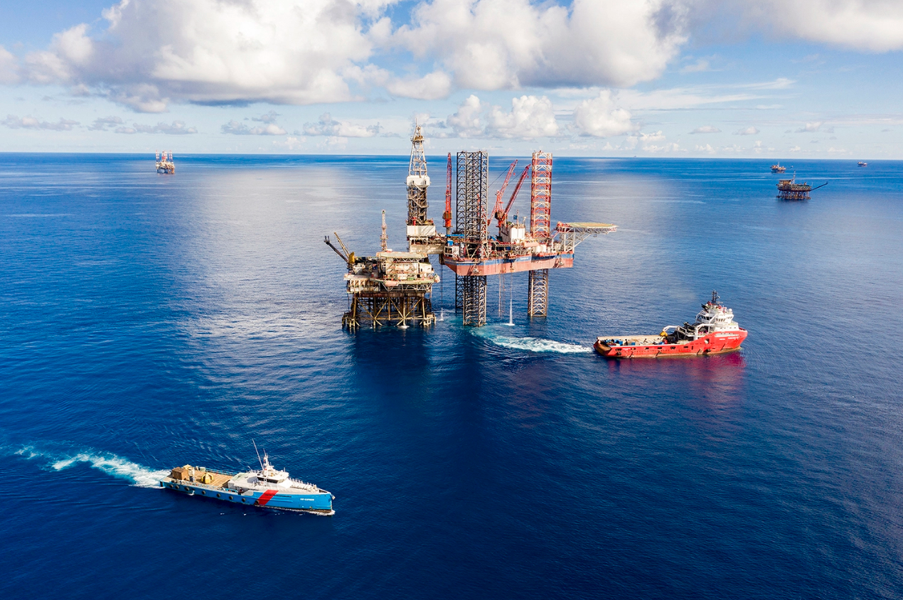 A boat in the water with a drilling rig  Description automatically generated