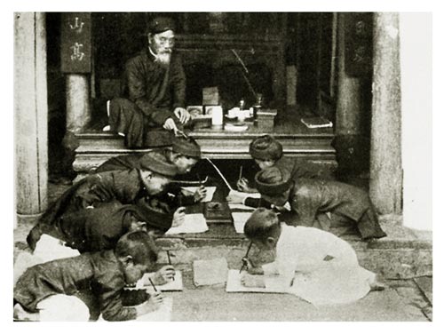 Thầy cầm roi, ngồi tr&ecirc;n sạp gụ chỉ dẫn học tr&ograve; viết chữ Nho. Theo Nho gi&aacute;o ng&agrave;y xưa, học sinh phải k&iacute;nh trọng thầy gi&aacute;o hơn cha mẹ, thầy chỉ sau vua, theo thứ bậc 