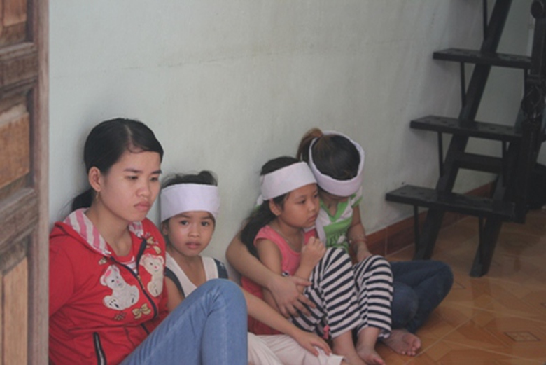 B&eacute; g&aacute;i 7 tuổi (&aacute;o đỏ, quần sọc) rầu rĩ b&ecirc;n x&aacute;c mẹ v&agrave; em