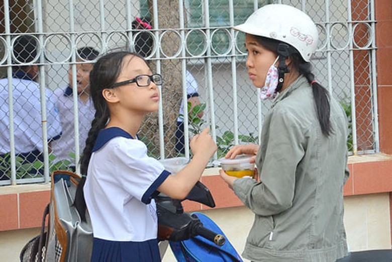 Một phụ huynh tranh thủ cho con ăn bữa chiều trước giờ học th&ecirc;mẢnh: NLĐ