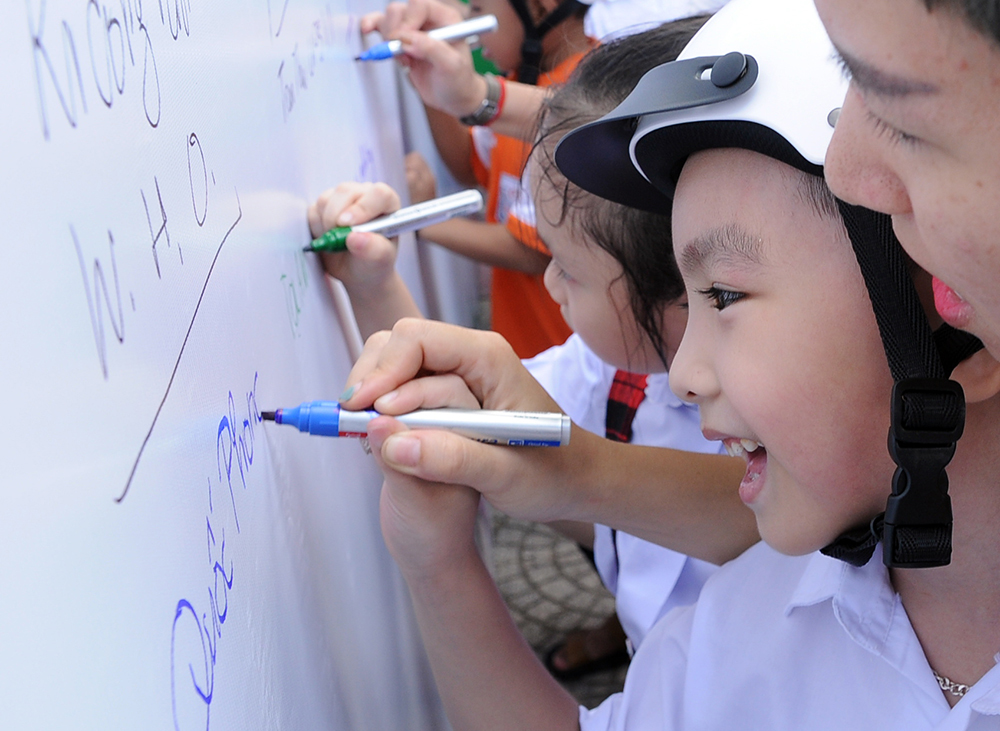Bé Quốc Phong nắn nót viết tên mình lên tấm bảng lớn với những mong ước được vui chơi, học hành trong môi trường an toàn, văn minh.