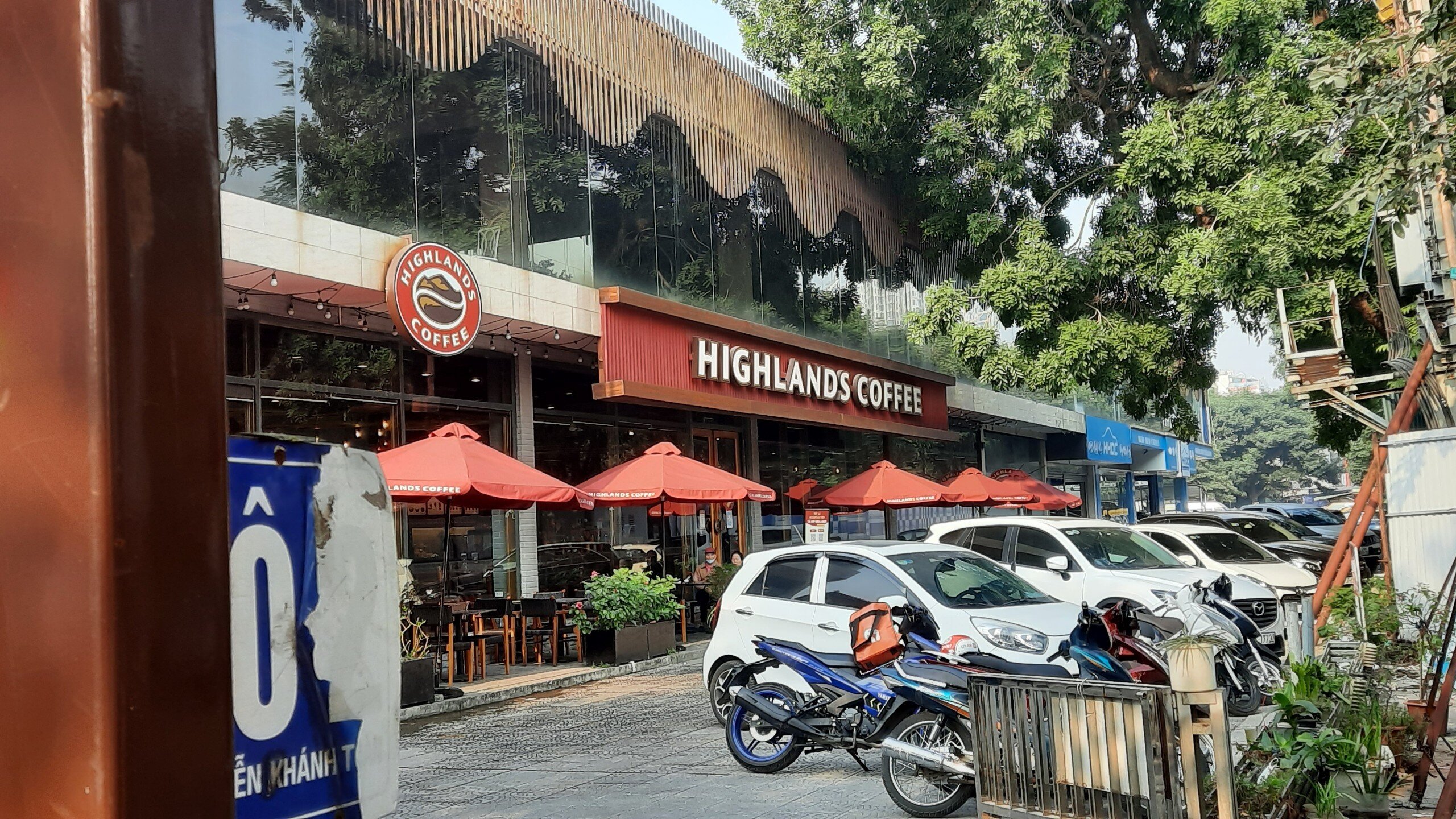 Ngay cạnh đ&oacute; l&agrave; qu&aacute;n c&agrave; ph&ecirc; treo biển Highlands Coffee vẫn hoạt động với người ra v&agrave;o thường xuy&ecirc;n.