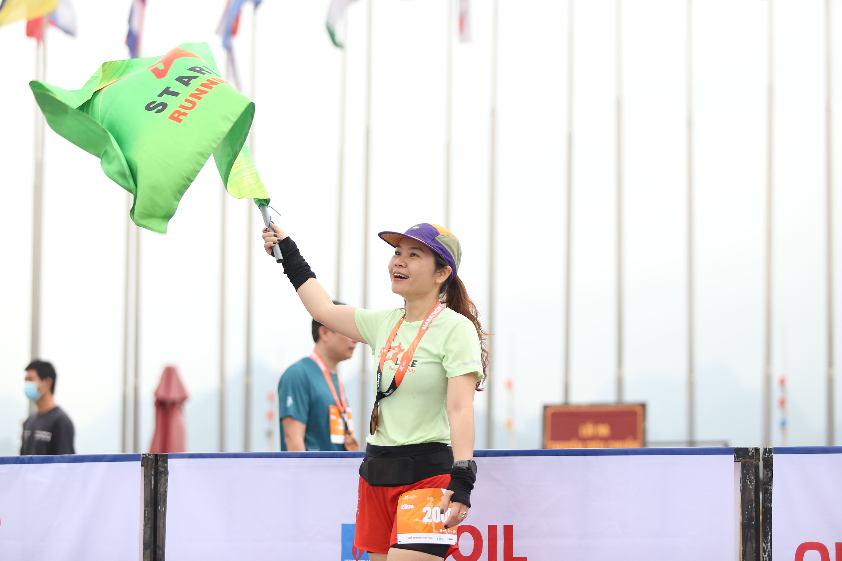 Một vận động vi&ecirc;n về đ&iacute;ch trước vẫy cờ ch&agrave;o đ&oacute;n những người ho&agrave;n th&agrave;nh qu&atilde;ng đường chạy sau m&igrave;nh.