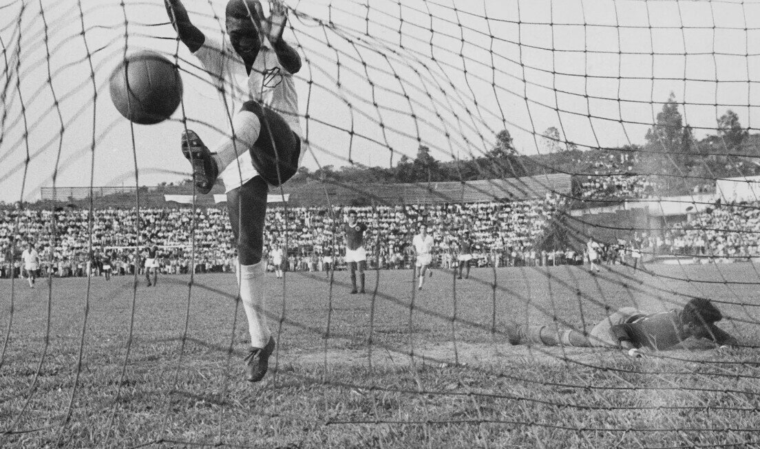 Pele nhảy vào lưới ăn mừng sau khi ghi bàn cho Santos trong trận đấu với Guarani của Paraguay năm 1958. Năm 1957, Pele có lần đầu tiên khoác áo đội tuyển quốc gia khi là cầu thủ ghi nhiều bàn thắng nhất trong giải vô địch bang Sao Paulo với 58 bàn. Ảnh: Getty Images