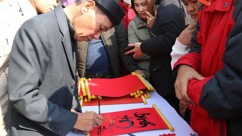 Du khách chăm chú xem nghệ nhân viết chữ.