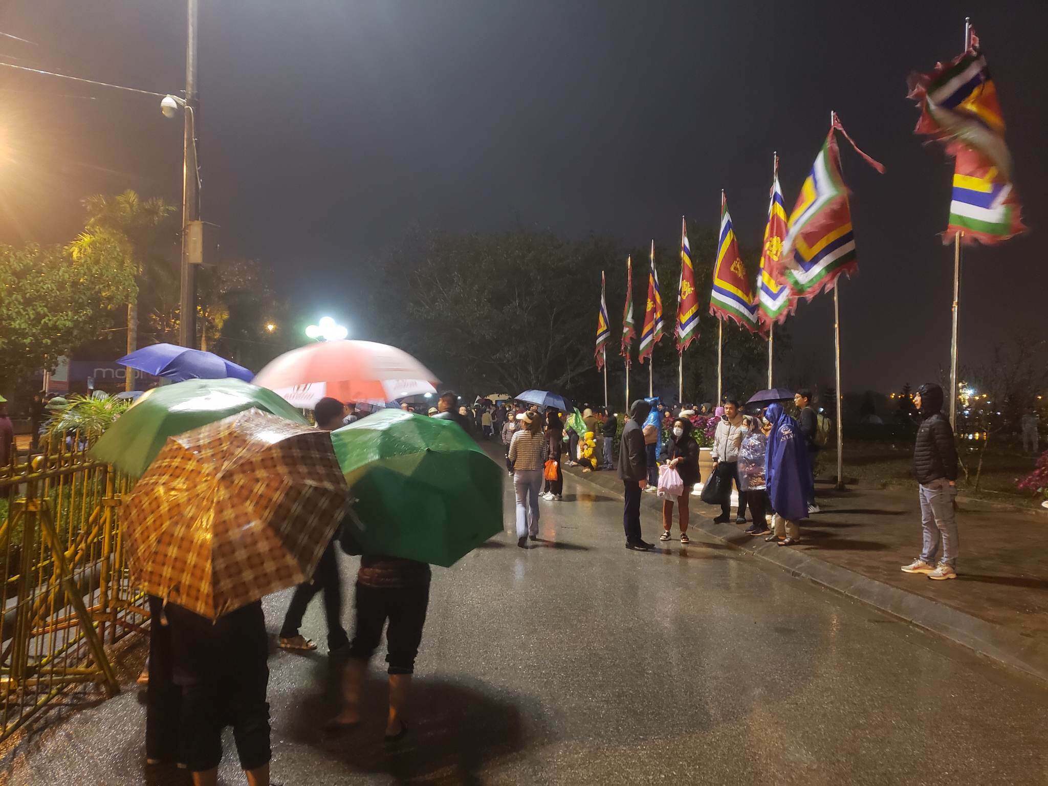 Sau 20h, tiết trời mưa nặng hạt, người d&acirc;n vẫn che &ocirc; đứng ngo&agrave;i khu vực barie chờ gi&acirc;y ph&uacute;t được nhận l&aacute; ấn.