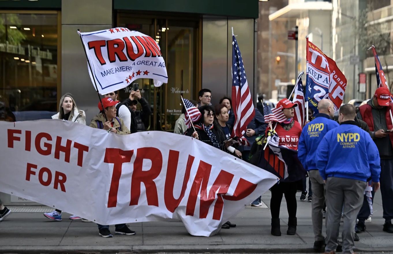 B&ecirc;n ngo&agrave;i, c&oacute; một nh&oacute;m nhỏ người biểu t&igrave;nh, đứng sau r&agrave;o chắn, mang biển hiệu, băng r&ocirc;n ch&agrave;o đ&oacute;n &ocirc;ng Trump. 
B&agrave; Susan Miller, một người d&acirc;n New York, 35 tuổi chia sẻ b&agrave; đến đ&acirc;y để ủng hộ &ocirc;ng Donald Trump v&igrave; tin &ocirc;ng v&ocirc; tội.