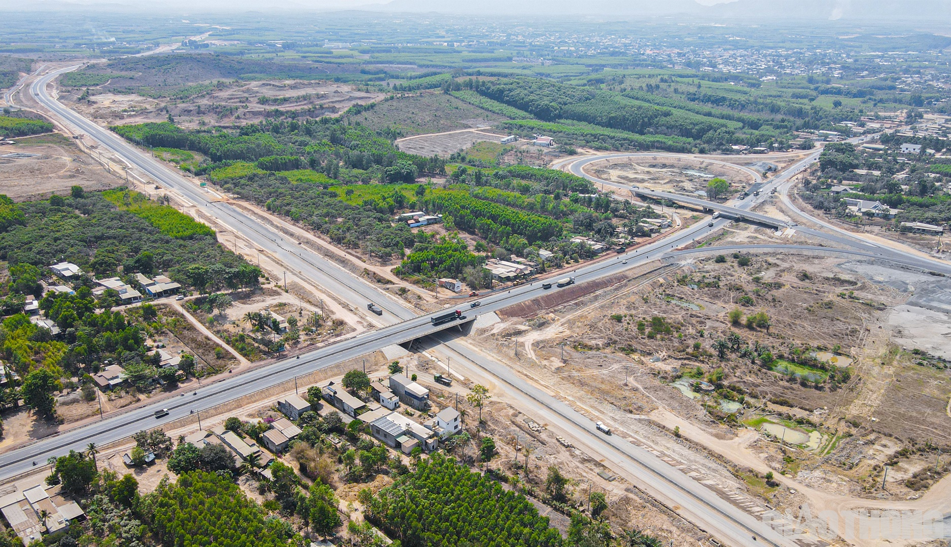 Nhớ lại thời gian đầu bắt tay v&agrave;o thi c&ocirc;ng, đại diện C&ocirc;ng ty TNHH Thương mại v&agrave; X&acirc;y dựng Trung Ch&iacute;nh chia sẻ, kh&oacute; khăn nhất l&agrave; l&uacute;c cao điểm g&aacute;c dầm v&agrave;o đ&uacute;ng m&ugrave;a mưa, c&aacute;c vị tr&iacute; thi c&ocirc;ng cầu nằm ở s&acirc;u trong đồi n&uacute;i, kh&oacute; tiếp cận. G&oacute;i thầu lại kh&ocirc;ng c&oacute; đường c&ocirc;ng vụ, việc vận chuyển những thanh dầm Super-T nặng đến 80 tấn từ b&atilde;i đ&uacute;c (c&aacute;ch c&ocirc;ng trường khoảng 40 km) phải di chuyển tr&ecirc;n tuyến ch&iacute;nh đang trong giai đoạn thi c&ocirc;ng nền, cứ mưa l&agrave; s&igrave;nh lầy. Nh&agrave; thầu phải canh thời tiết từng ng&agrave;y, vừa đi vừa c&oacute; m&aacute;y x&uacute;c, m&aacute;y đ&agrave;o đi theo, chỗ n&agrave;o s&igrave;nh lầy sẽ phải hỗ trợ kịp thời. Trong ảnh: N&uacute;t giao cao tốc Phan Thiết - Dầu Gi&acirc;y với QL1A