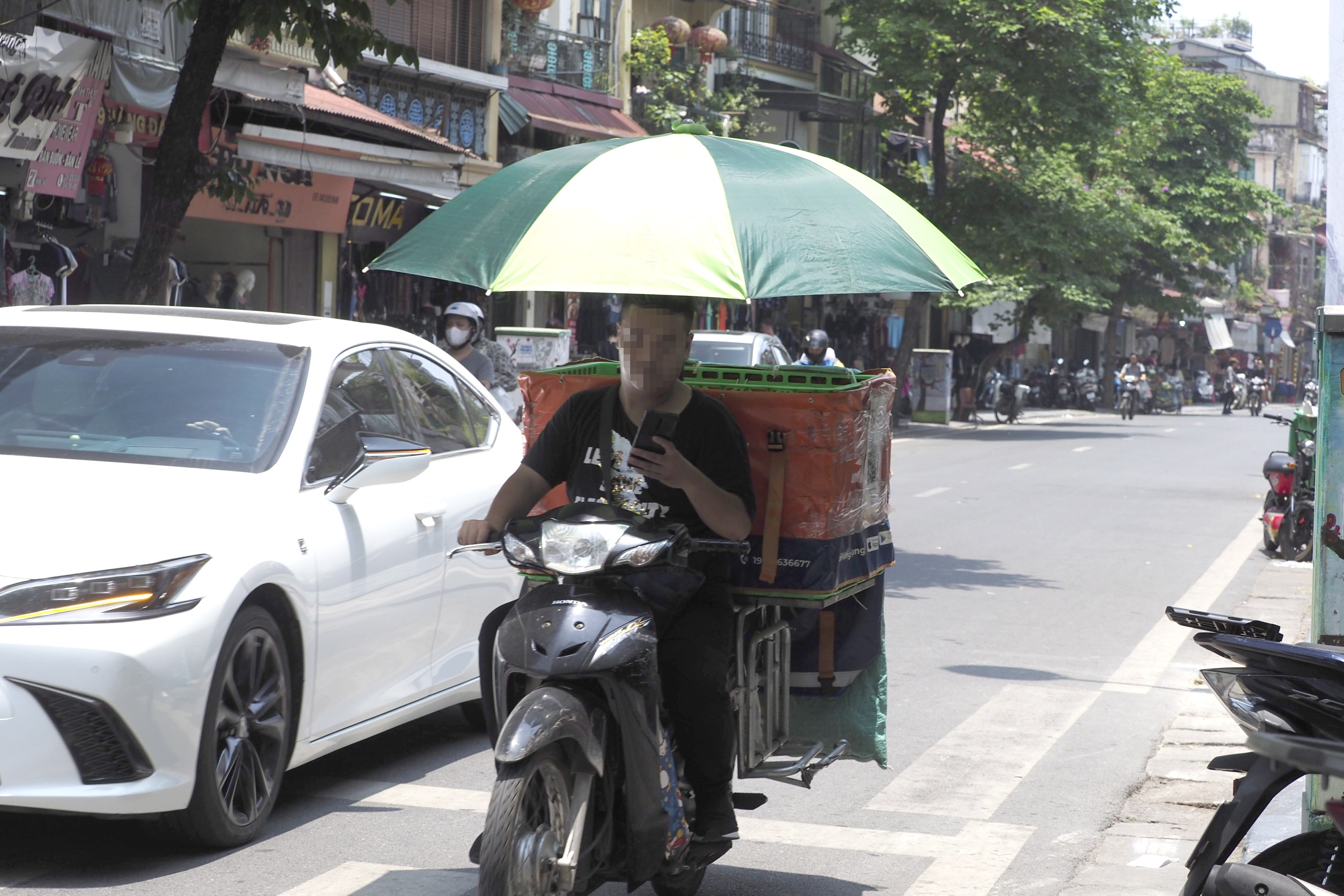 Người đ&agrave;n &ocirc;ng l&agrave;m nghề shipper n&agrave;y đ&atilde; sử dụng chiếc &ocirc; để chống chọi với c&aacute;i nắng đầu m&ugrave;a.