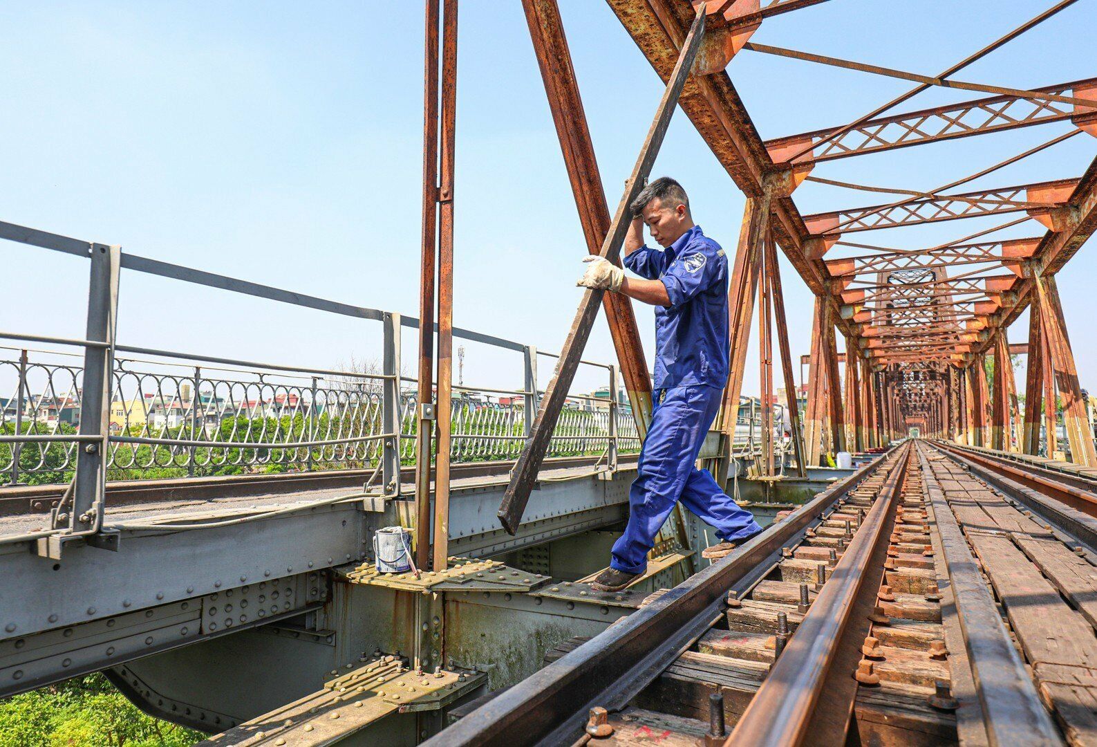 Anh Hiệp, người c&ugrave;ng nh&oacute;m sản xuất với anh Thuỷ cho hay, để vẫn ho&agrave;n th&agrave;nh c&ocirc;ng việc, đồng thời tr&aacute;nh bớt nắng n&oacute;ng, c&aacute;c anh l&agrave;m từ 6h00 s&aacute;ng. Mỗi nh&oacute;m được giao kho&aacute;n phụ tr&aacute;ch một đoạn, cứ thế c&aacute;c nh&oacute;m tập trung sơn, l&agrave;m đến tận trưa, đến khi n&agrave;o ho&agrave;n th&agrave;nh mới th&ocirc;i. Ảnh: Anh Thuỷ chuẩn bị c&aacute;c thanh g&aacute; trước khi v&agrave;o vị tr&iacute; sơn ph&iacute;a dưới mặt cầu