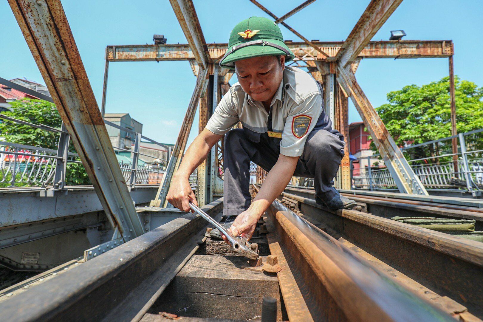 Tham gia bảo đảm an to&agrave;n cho cầu Long Bi&ecirc;n c&ograve;n lực lượng tuần g&aacute;c. Anh Đ&agrave;o Minh Dực, c&ocirc;ng nh&acirc;n tuần cầu cho biết, anh đ&atilde; l&agrave;m c&ocirc;ng nh&acirc;n tuần cầu tr&ecirc;n 10 năm. H&agrave;ng ng&agrave;y, sau khi nhận ban l&uacute;c 6h, anh phải đi tuần dọc theo đường sắt tr&ecirc;n cầu, vừa đi vừa quan s&aacute;t đường sắt v&agrave; cả đường bộ xem c&oacute; xảy ra vấn đề g&igrave; uy hiếp đến an to&agrave;n kh&ocirc;ng để xử l&yacute; kịp thời. Ảnh: Anh Dực siết lại bu l&ocirc;ng giữ t&agrave; vẹt bị lỏng giữa nắng gắt