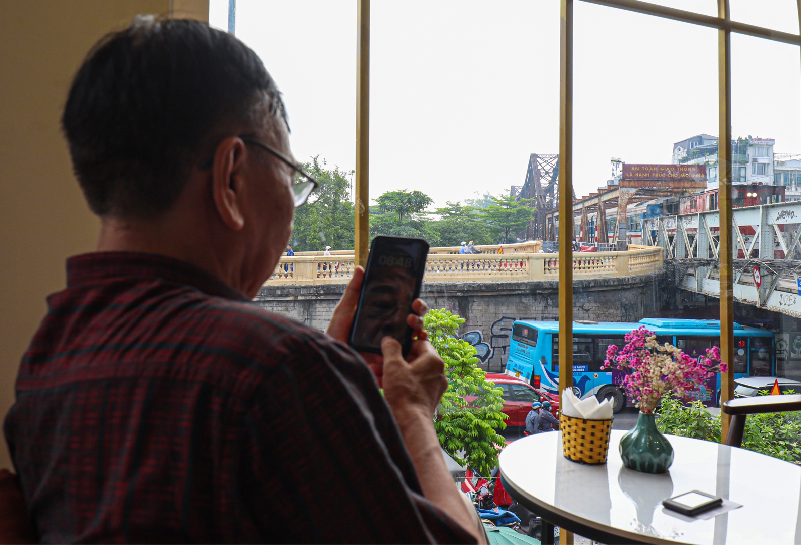 Ở một g&oacute;c kh&aacute;c ph&ograve;ng đợi, kh&aacute;ch c&oacute; thể ngắm nh&igrave;n c&acirc;y cầu Long Bi&ecirc;n hơn trăm tuổi, biểu tượng cho lịch sử, văn h&oacute;a, c&ocirc;ng tr&igrave;nh giao th&ocirc;ng Thủ đ&ocirc;. V&agrave; đương nhi&ecirc;n kh&ocirc;ng thể bỏ qua gi&acirc;y ph&uacute;t đo&agrave;n t&agrave;u từ từ chạy qua cầu Long Bi&ecirc;n. Ảnh: Một nam h&agrave;nh kh&aacute;ch lớn tuổi vội ghi lại h&igrave;nh ảnh t&agrave;u qua cầu trong khi chờ t&agrave;u tại đ&acirc;y