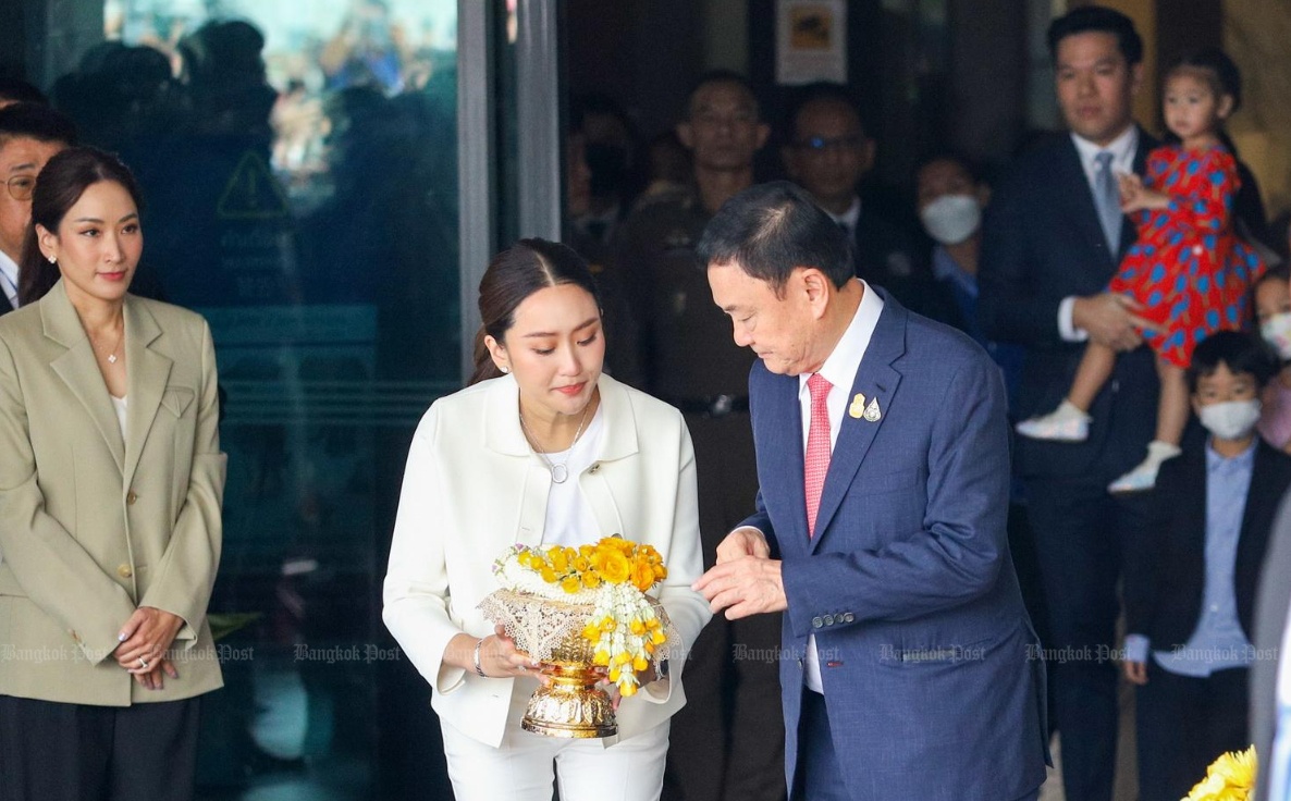 &Ocirc;ng Thaksin mặc bộ comple m&agrave;u xanh đậm, đeo c&agrave; vạt m&agrave;u hồng đi ra ngo&agrave;i cửa nh&agrave; ga d&agrave;nh cho m&aacute;y bay ri&ecirc;ng c&ugrave;ng ba con Panthongtae, Pintongta v&agrave; Paetongtarn.